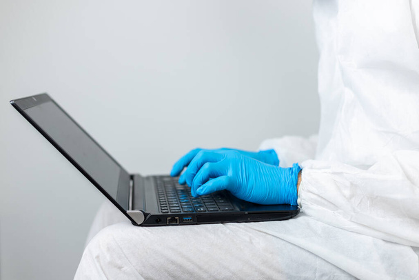Forscher arbeitet mit seinem Laptop in Covid-19 Coronavirus-Schutzkleidung - Foto, Bild