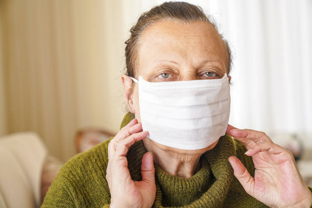 Portret starszej kobiety noszącej maskę chirurgiczną do ochrony przed wirusem korony. Babcia siedzi w salonie i patrzy w górę  - Zdjęcie, obraz
