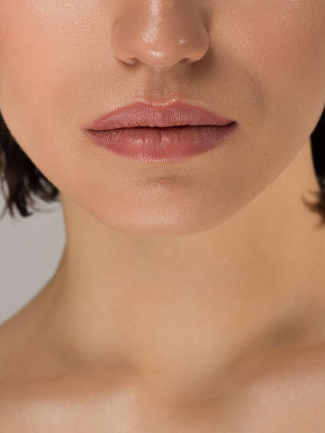 Close-up of woman's lips with fashion natural beige lipstick makeup. Macro sexy pale lipgloss make-up . Gentle pure skin and wavy blonde hair. Cosmetology, Spa, increase in lips. Face powder - Photo, image
