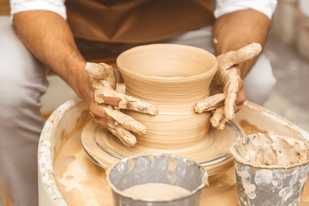 A young male potter works in his workshop on a potters wheel and makes clay products. Close-up of hands - Foto, Bild