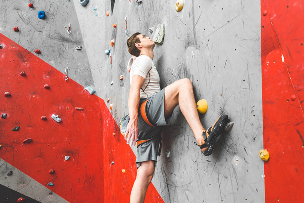 Sportsman climber moving up on steep rock, climbing on artificial wall indoors. Extreme sports and bouldering concept - Фото, изображение