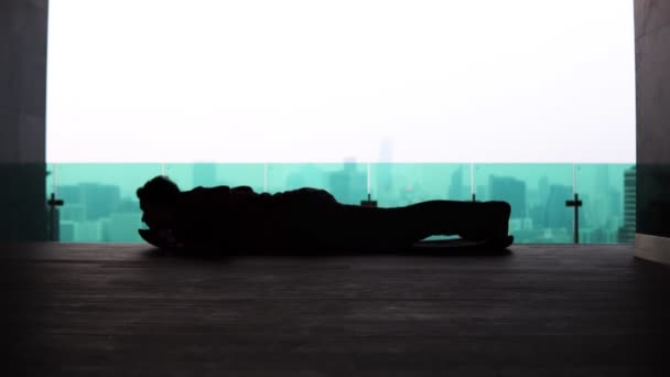 Σιλουέτα ενός άνδρα κάνει κάμψεις από το πάτωμα στην οροφή ενός κτιρίου με φόντο την μητρόπολη - Πλάνα, βίντεο