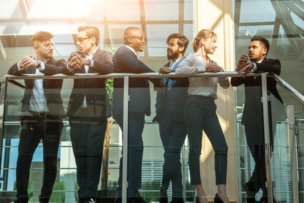 young business people are standing and talking on the background of glass offices. Corporate businessteam and manager in a meeting. - Foto, Imagen