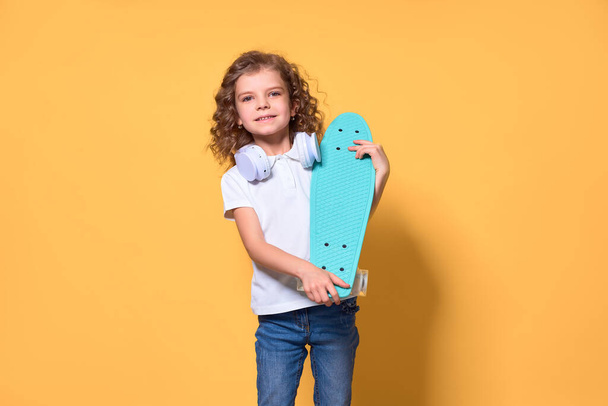 Active and happy Kid having fun with penny board, smiling face stand skateboard. Penny board cute skateboard for girls. Lets ride. Girl ride penny board yellow background. Summer vacation - Foto, Bild