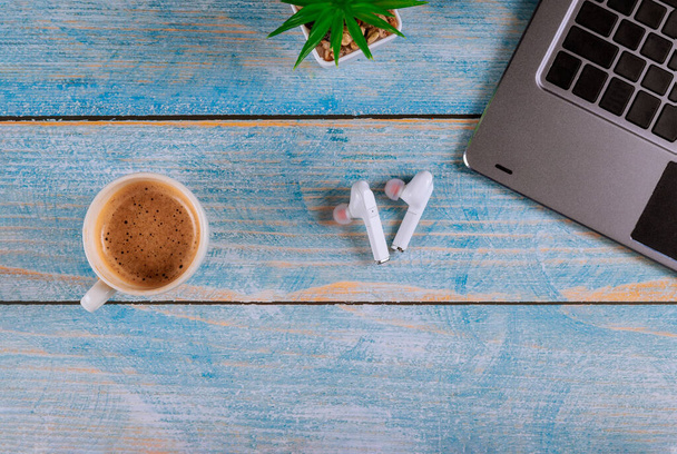 Стол в рабочем месте офисное оборудование беспроводные наушники в чашке кофе эспрессо вид сверху, плоский лежал
 - Фото, изображение