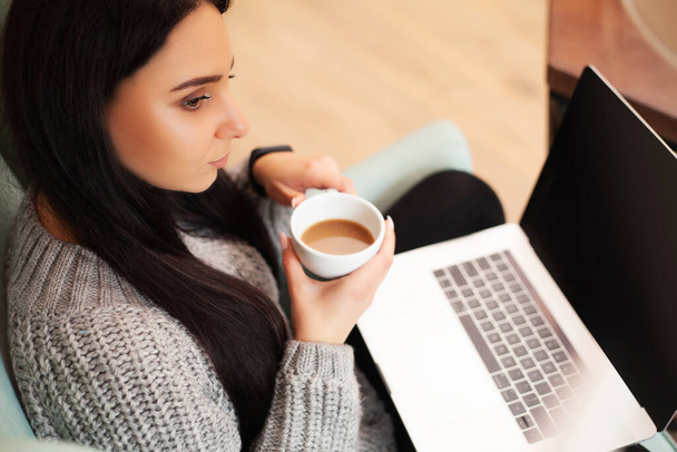 Cute woman stay at home and working at a laptop drinking coffee - Photo, Image