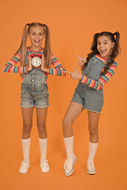 Timing personal plan and schedule. Counting time concept. Dead line. Happy little girls hold vintage alarm clock on orange background. Small children smiling with mechanical clock. School clock - Фото, зображення