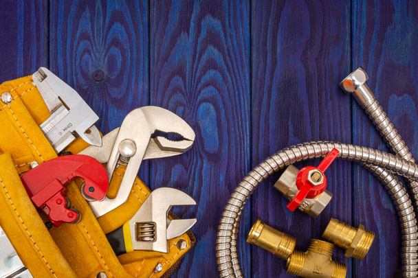 Des outils de plomberie dans un sac jaune et des pièces de rechange sur des planches de bois bleues sont utilisés pour remplacer ou réparer
 - Photo, image