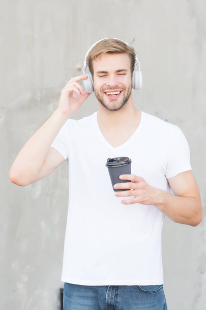 His morning is dedicated to music. Happy guy listen to music drinking coffee. Handsome man wear headphones playing music. New technology. Modern life. Fun and entertainment. Music and takeaway drink - Photo, Image
