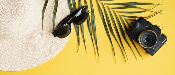 Summer background with beach straw hat, sunglasses, palm leaf and camera. Stylish traveler accessories on yellow background, top view, flat lay - Photo, image