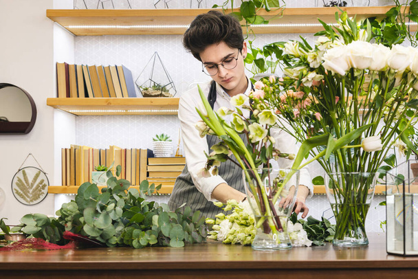 Attractive young male florist with glasses and apron works in a flower shop. - Foto, Imagem