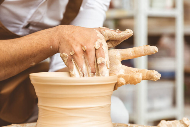 A young male potter works in his workshop on a potters wheel and makes clay products. Close-up of hands - Фото, зображення