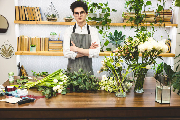 Atraente jovem florista masculino com óculos e avental funciona em uma loja de flores
. - Foto, Imagem