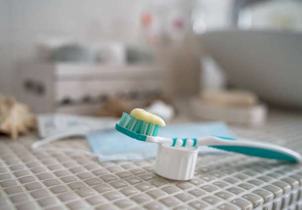 Offene Zahnpasta, eine Zahnbürste und eine aus dem Gesicht entfernte medizinische Maske liegen auf dem Tisch vor dem Waschbecken im Badezimmer.. - Foto, Bild