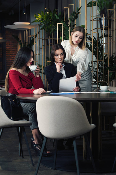 Las mujeres de negocios en ropa casual inteligente están discutiendo asuntos, tomando café y sonriendo mientras trabajan juntas en el café.
. - Foto, imagen