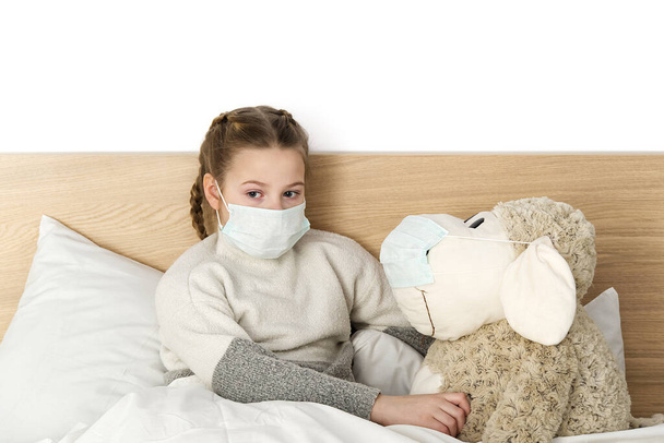 Un enfant malade et triste dans un masque avec une température et un mal de tête se trouve au lit. Grippe rhume bactérie du virus de la maladie. fille avec jouet dans la chambre à coucher porter un masque de protection, Protéger contre le Coronavirus concept
 - Photo, image
