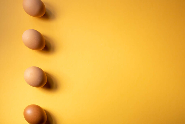 Row of raw eggs aligned on yellow background. Easter concept. Space for text - Fotoğraf, Görsel