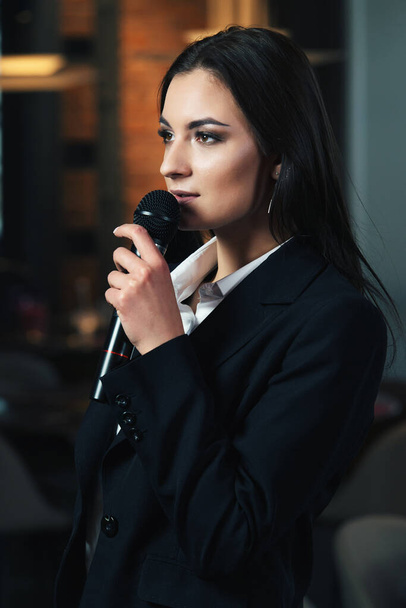 Argomento aziendale e del discorso: donna in camicia bianca con microfono nero, indoor
 - Foto, immagini