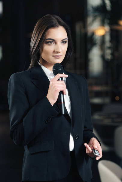 Liike-elämän ja puheen aihe: nainen valkoisessa paidassa, jossa musta mikrofoni, sisätiloissa
 - Valokuva, kuva