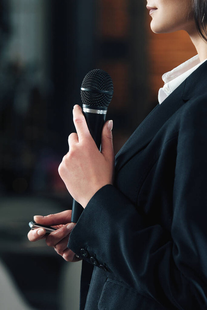 Business en spraak onderwerp: vrouw in een wit shirt met een zwarte microfoon, indoor - Foto, afbeelding