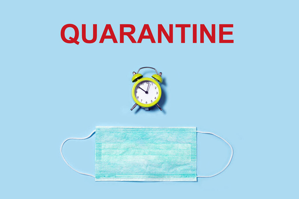 Word QUARANTINE, Disposable mask against and clock on blue background. Flat lay and copy space. Concept of coronavirus quarantine. - Valokuva, kuva