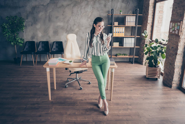 Full size photo of positive smart leader business lady girl use smartphone texting typing chatting with startup partners wear striped shirt mint color pants stand in workplace workstation - Fotografie, Obrázek