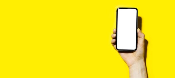 Primer plano del teléfono inteligente de mano masculino con maqueta sobre fondo panorámico de color amarillo con espacio para copiar
. - Foto, imagen
