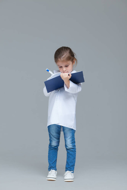 Adorable child girl uniformed as doctor is writing medical record isolated on grey background - Fotoğraf, Görsel