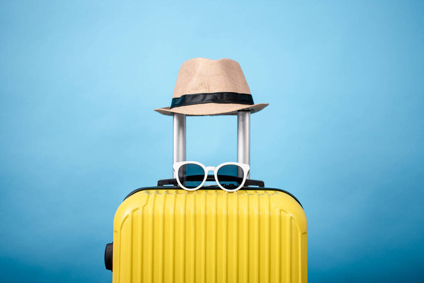 Yellow suitcase with hat and sunglasses on a blue background. - Valokuva, kuva