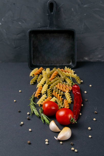 Итальянская еда сырые макароны с помидорами, розмарином, острым перцем и чесноком в небольшой сковороде. Виды сверху, крупным планом
 - Фото, изображение