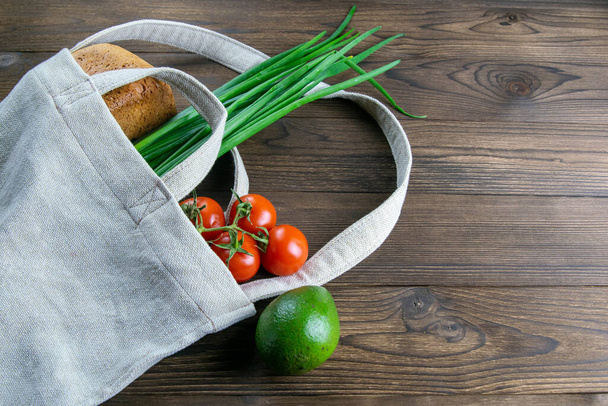 Woven bag of different health food on dark wooden table background. Bread, green onion, garlic, tomato and yellow peper. Top view with clear space. - Photo, Image