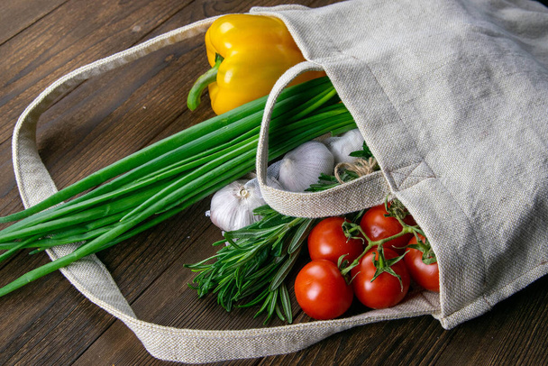 Geweven zak van verschillende gezondheid voedsel op donker houten tafel achtergrond. Groene ui, knoflook, tomaat en gele peper. Bovenaanzicht met duidelijke ruimte. - Foto, afbeelding