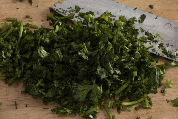 Cuchillo de chef-kok cortando cilantro en casa para preparar comida casera con trapo de rayas - Foto, afbeelding
