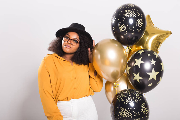 Holidays, birthday party and fun concept - Portrait of smiling young African-American young woman looking stylish on white background holding balloons. - Photo, Image