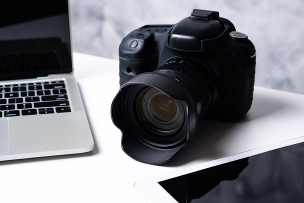 Una fotocamera digitale nera, un tablet e un computer portatile su un tavolo
. - Foto, immagini