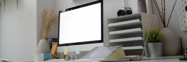 最小限のオフィスルームでは、空白の画面コンピュータ、タブレット、オフィス用品や装飾品とオフィスデスクの切り取られたショット  - 写真・画像