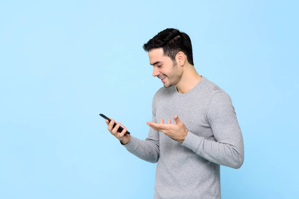 Lachende gelukkige jongeman met behulp van smartphone geïsoleerd op lichtblauwe studio achtergrond - Foto, afbeelding