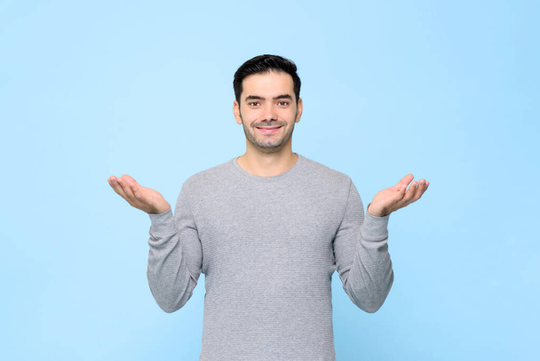 Puolikas vartalo muotokuva hymyilevä mies harmaa t-paita avoin käsi ele vaaleansininen studio tausta
 - Valokuva, kuva