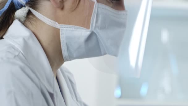 Pielęgniarka pracująca nad zestawami do testów koronawirusowych w laboratorium medycznym nosząca tarczę i maskę. - Materiał filmowy, wideo