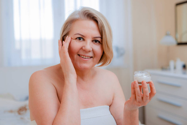Oudere vrouw anti-aging lotion tegen donkere kringen onder de ogen. Happy Mature vrouw gebruikt cosmetische crème om rimpels te verbergen. Een dame met een dagcrème. - Foto, afbeelding
