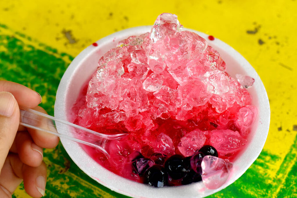 Süß rasiertes Eis in Schaumstoffbecher auf buntem gelb-grünem Tisch. Berühmtes Thai-Dessert im Sommer. - Foto, Bild