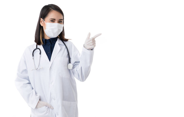 外科衛生保護マスクを着用した医療女性。若いアジア人医師女性。専門家フレンドリーな女の子医師でラボコートドレス指差し指へ空白のコピースペース. - 写真・画像