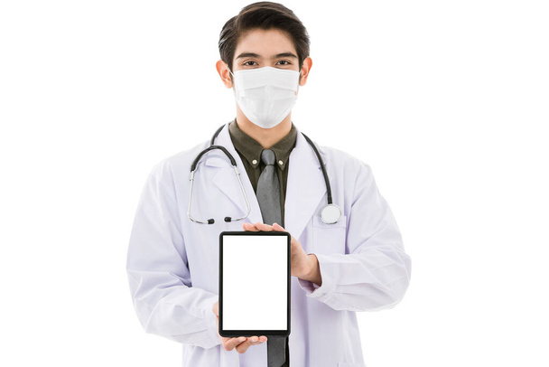 Junge und gut aussehende, smarte asiatische Ärztin mit chirurgischer Hygieneschutzmaske isoliert auf weißem Hintergrund und mit einem leeren Kopierbildschirm in der Hand. Idee für Mediziner. - Foto, Bild