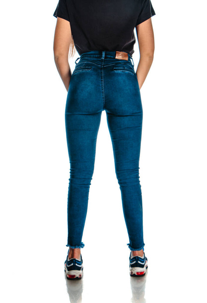 Portrét modelky pózující v módních džínových kalhotách a stylových teniskách - Fotografie, Obrázek