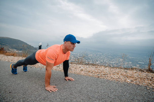 Γυμνασμένος μεσήλικας που φοράει αθλητικά ρούχα ετοιμάζεται για τρέξιμο ενώ κάνει push up - Φωτογραφία, εικόνα