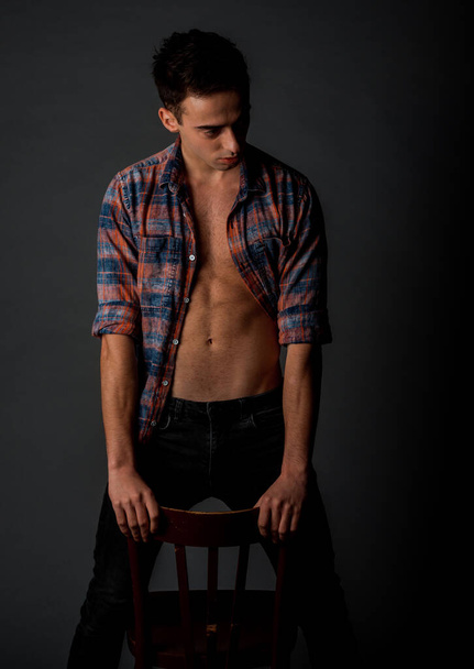 Attractive stylish man posing in black denim jeans against black wall - Photo, image