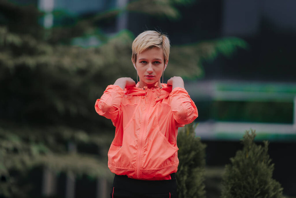 Portret van een aantrekkelijk fitnessmeisje in koptelefoons die stretching oefeningen doen in het park - Foto, afbeelding