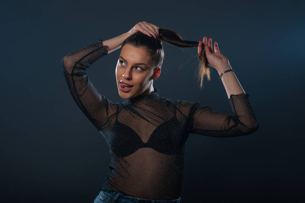 Fashion portrait of an attractive brunette girl holding and pulling her ponytail. - Photo, Image