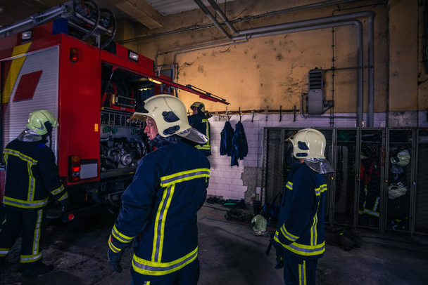 Feuerwehrleute bereiten ihre Uniform vor und das Feuerwehrauto im Hintergrund im Feuerwehrhaus - Foto, Bild