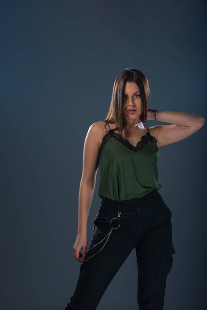 Portrait of a sexy young female model  standing in a studio and wearing dark green top and black pants - Zdjęcie, obraz